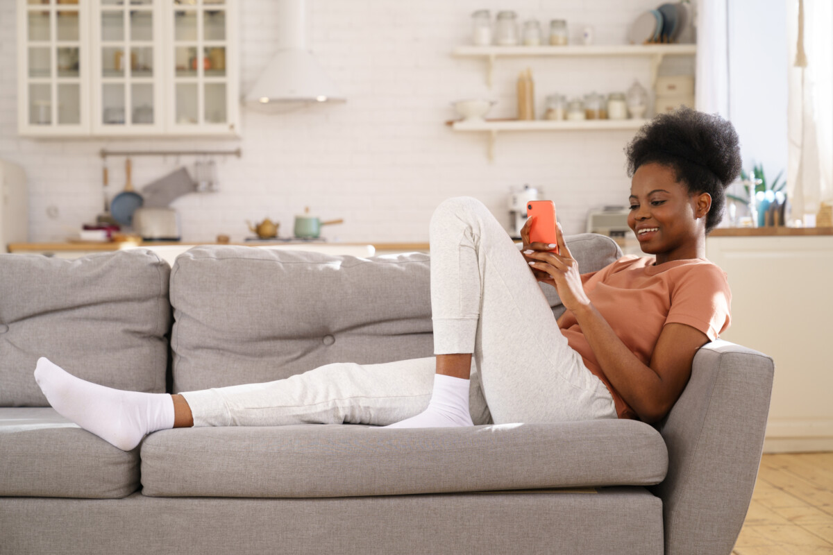 Woman relaxing on the couch in sweatpants looking at her smartphone