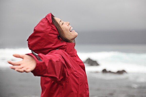 Woman wearing a rain jacket with arms outstretched at beach