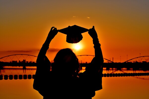 holding up a graduation cap to the sunset
