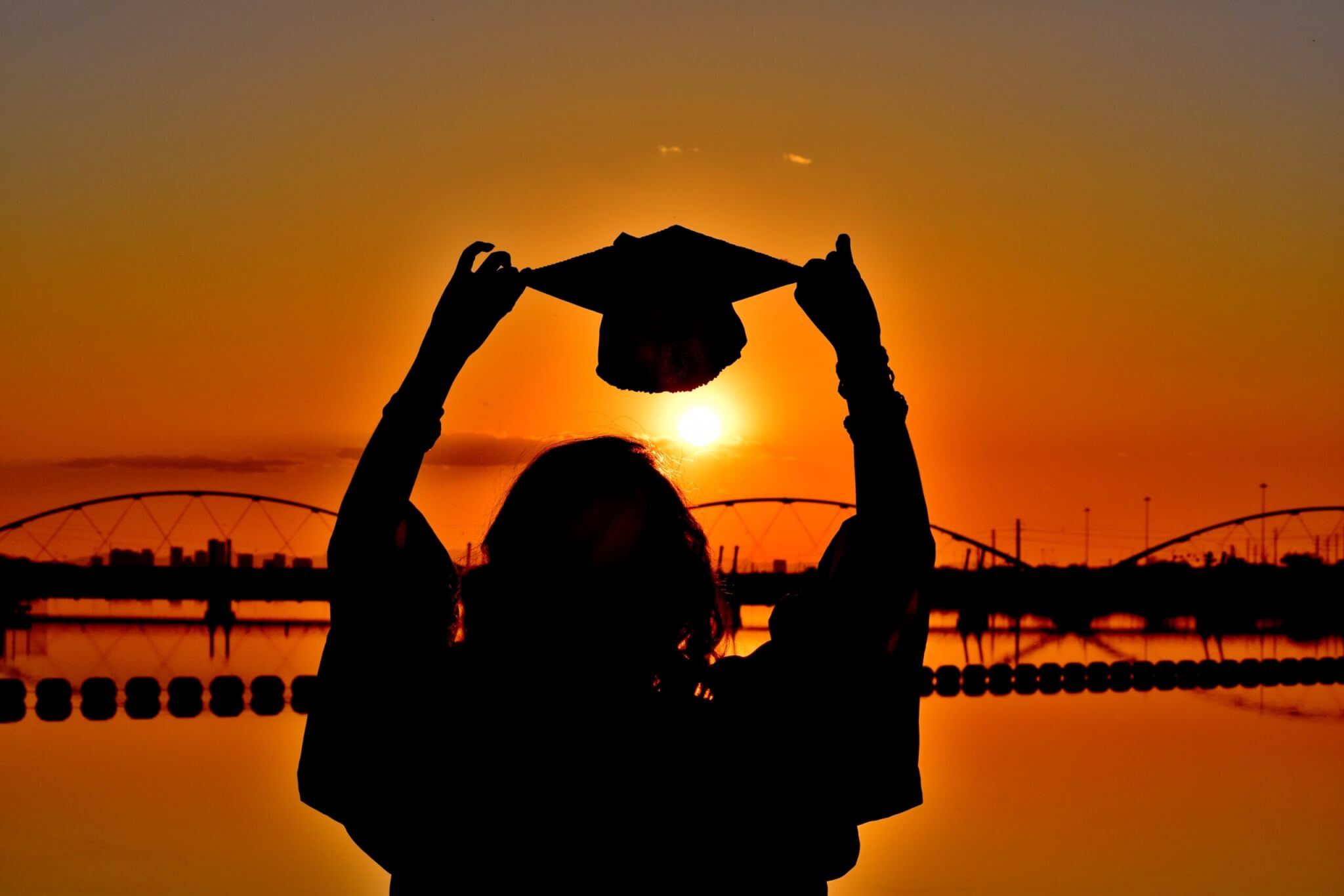holding up a graduation cap to the sunset