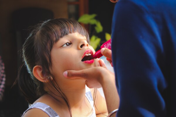 Adult puts lipstick on a young girl