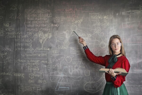 A strict teacher stands in front of a blackboard