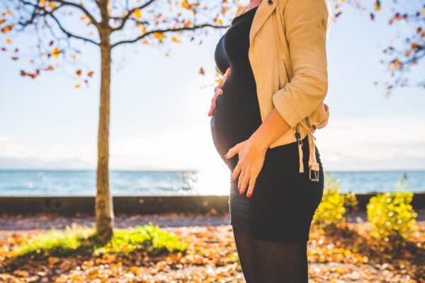 A pregnant woman standing in a park near the water