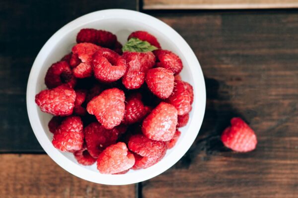 raspberries in white bowl on wood table