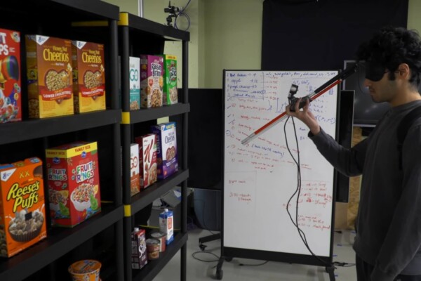 A man stands next to a store shelf to test a "smart" walking cane while blindfolded
