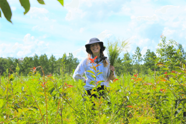 Researcher Caitlin Risener stands in grassy field with goldenrod plant
