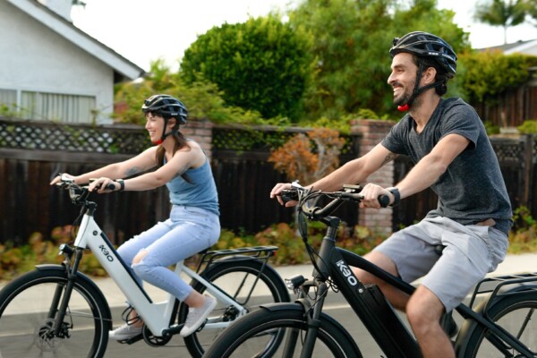 Two people smiling while riding bikes, wearing helmets