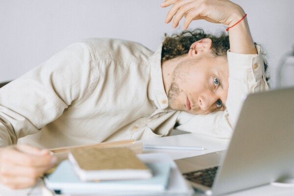 A man puts his head down on a desk next to a laptop