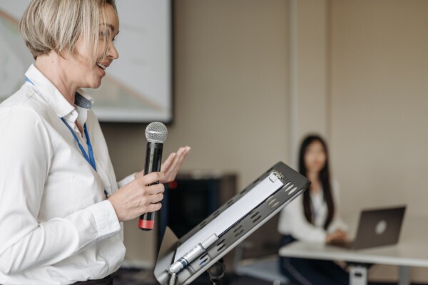 A woman stands with a microphone at a meeting