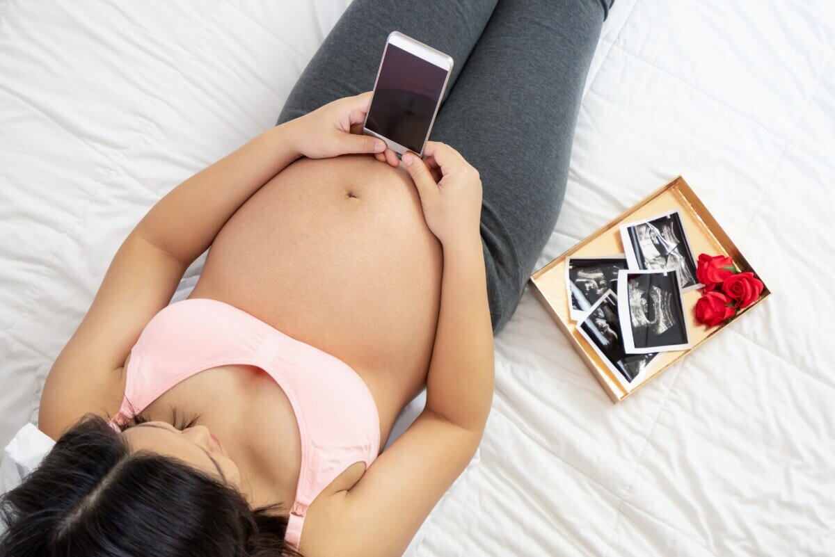 Pregnant woman looking at smartphone in bed
