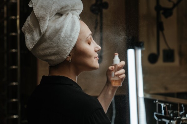 woman with towel on her head spraying mist on her face
