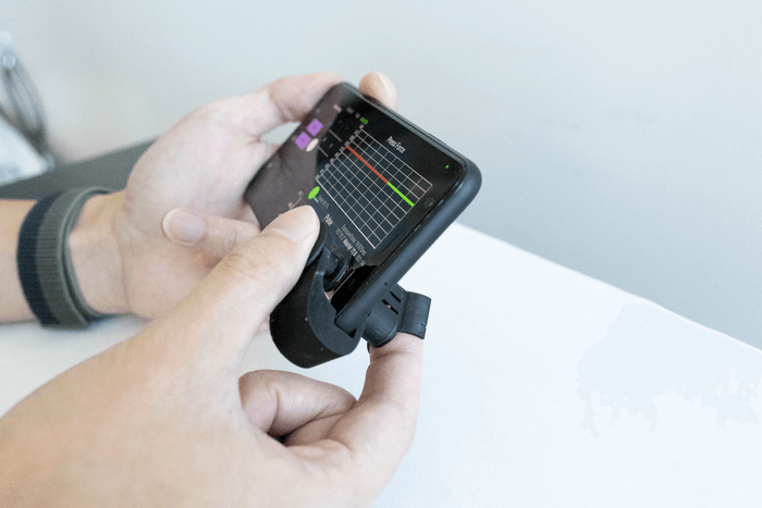 Two hands holding black prototype device of a blood pressure monitoring clip. 