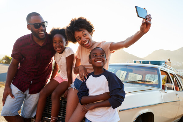 Family road trip: Parents take selfie with kids in front of car