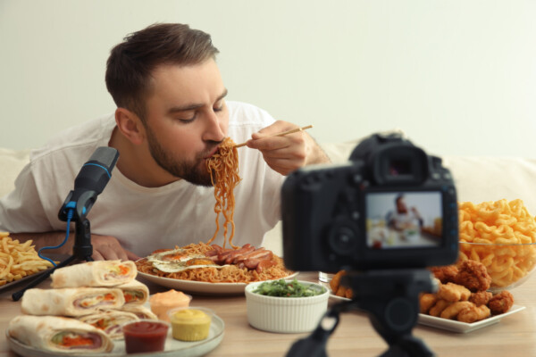 Mukbang video host slurps noodles amid plates of other unhealthy foods.