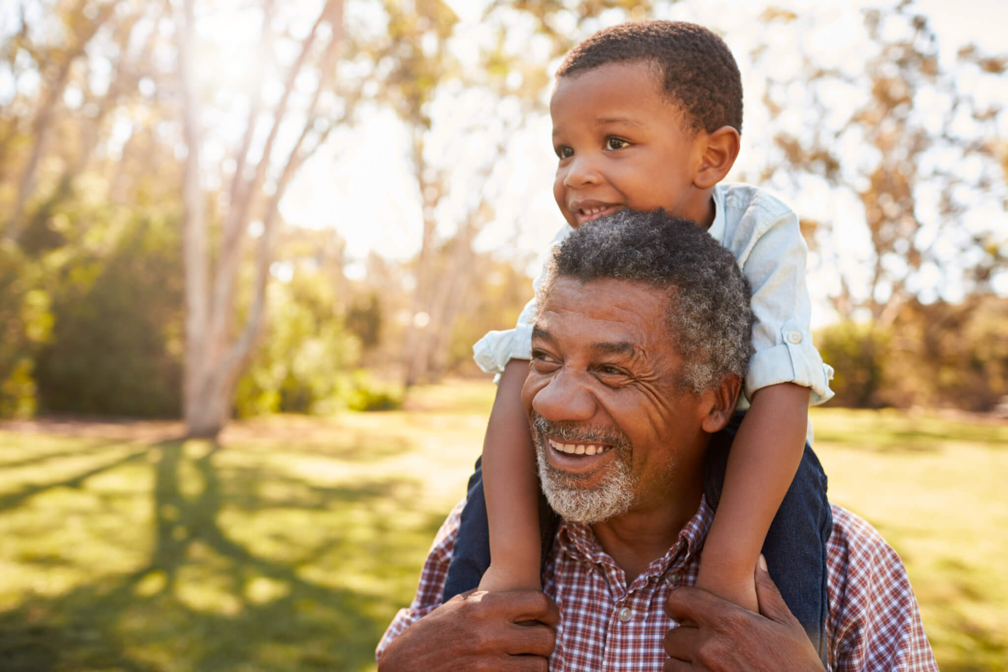 Older father or grandfather walks with a happy child on his shoulders