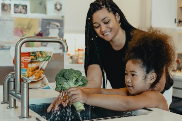 Mother and daughter washing broccoli in the kitchen sink