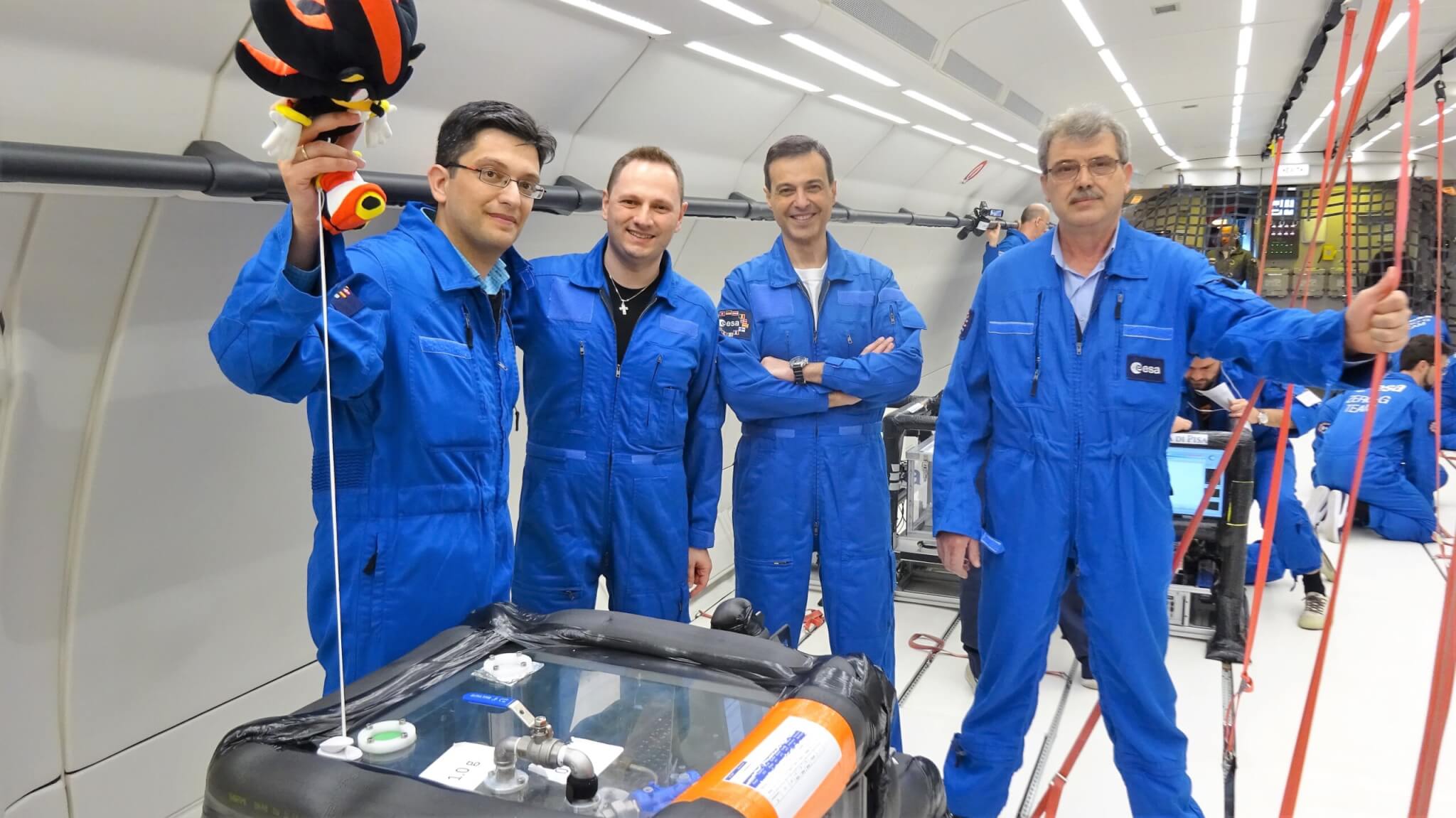4 men dressed in blue nasa suit standing around large tub for frying