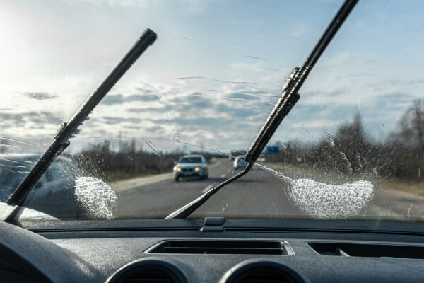 Car wipers clean windshields when driving in sunny weather, inside view.