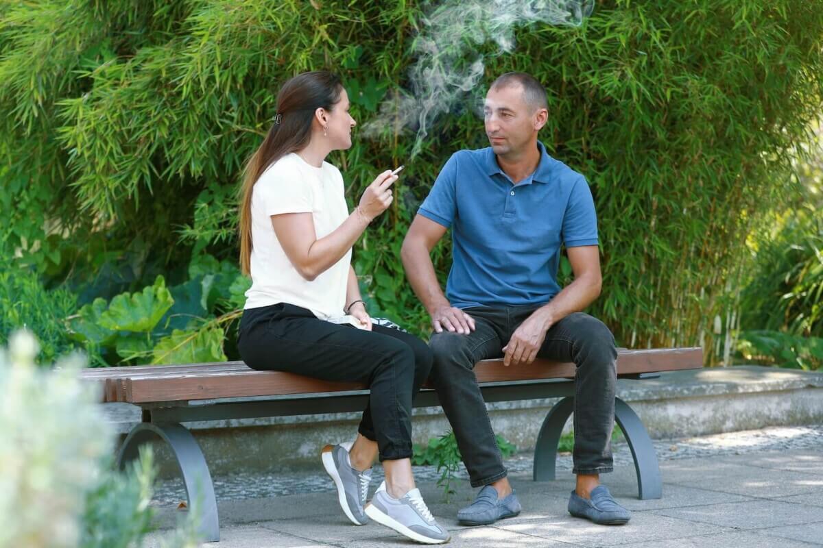 man and woman sitting on bench smoking