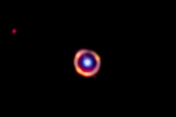 In this false-color Webb telescope image, the foreground galaxy is shown in blue, while the background galaxy is in red. The organic molecules are highlighted in orange.