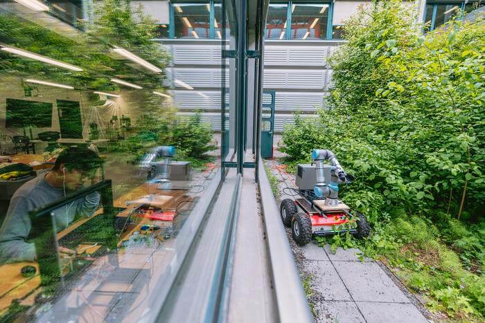 large robot with long arm, on wheels, roams test enviornment filled with greenery and vegetables