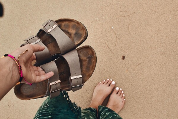 Someone holding a pair of Birkenstock sandals on the beach