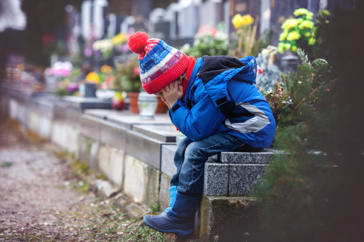 Sad boy sitting on a grave in a cemetery 