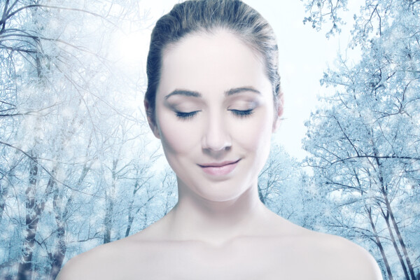 Head and shoulders of young woman with eyes closed over winter forest.