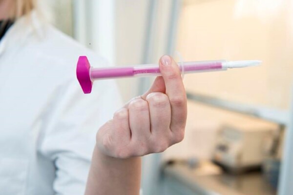 close up picture of a hand of person wearing a white jacket, holding up a pink plastic stick with a white tube