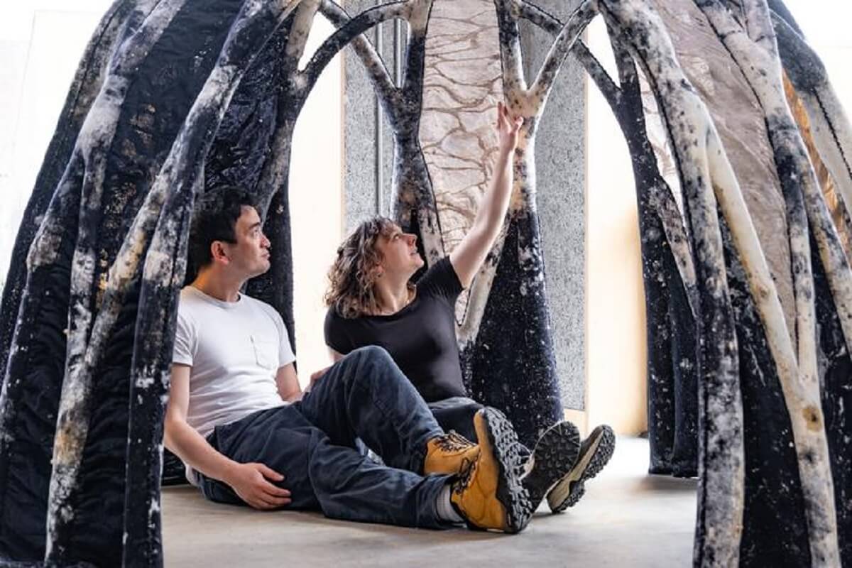 pic of large black and white dome, open in front with two people sitting inside,, made of fungus material