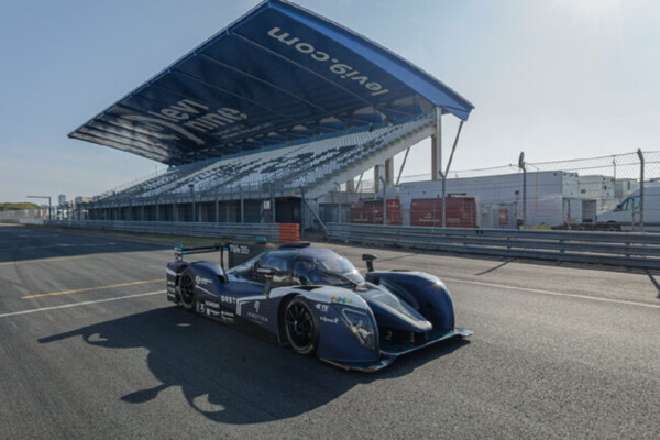 dark blue racecar with white striipes along the front of the body, parked on a race track in front blue and white grandstand