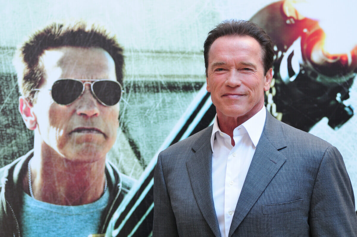Arnold Schwarzenegger standing in front of a poster for “The Last Stand” in 2013