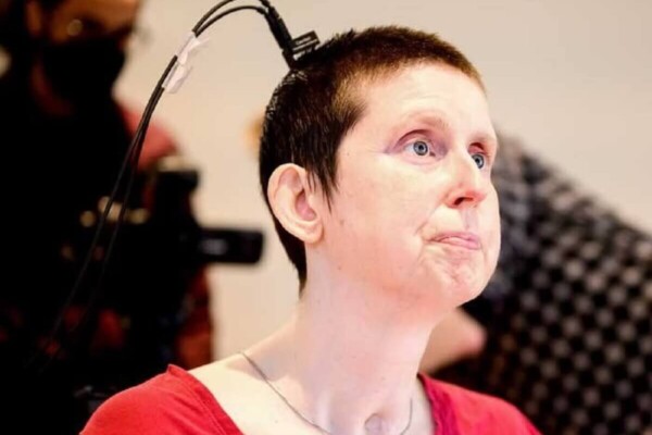 Woman wearing red shirt sitting in a chair with electrode attached to back of her head