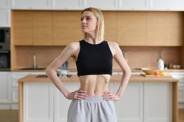 Skinny woman sucking in her belly and standing in the kitchen