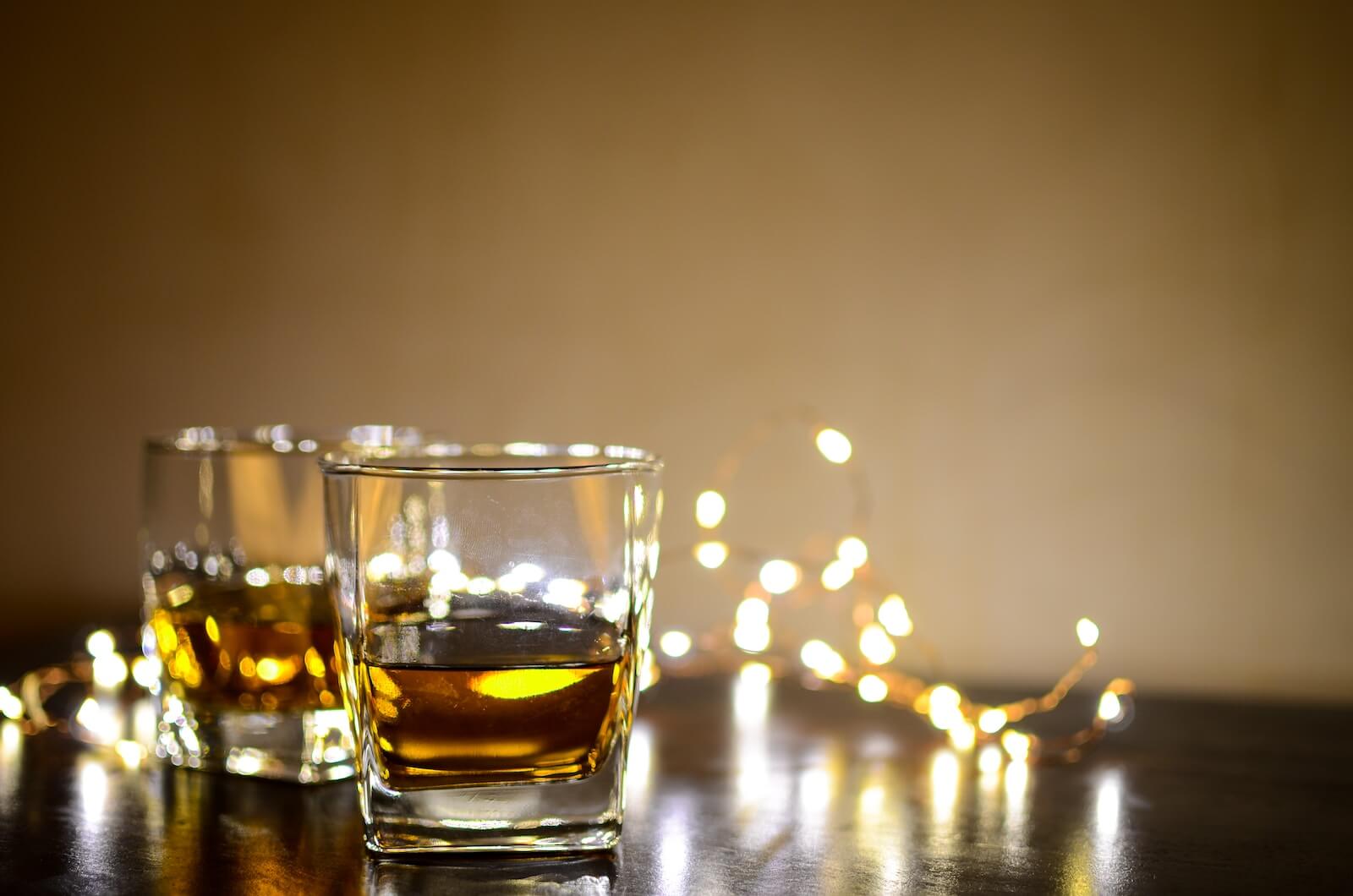 Two glasses of Scotch backlit by twinkle lights