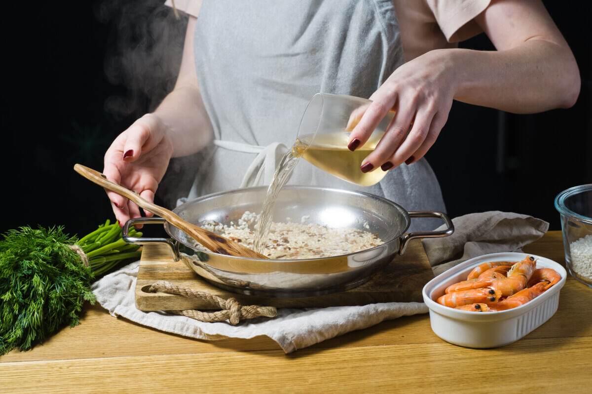 Someone adding white wine to a seafood risotto