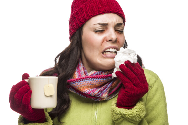 A sick woman drinking tea and sneezing