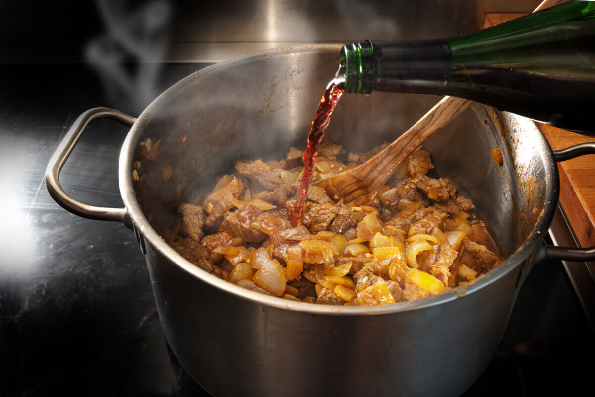 Someone pouring red wine into a pot of stew