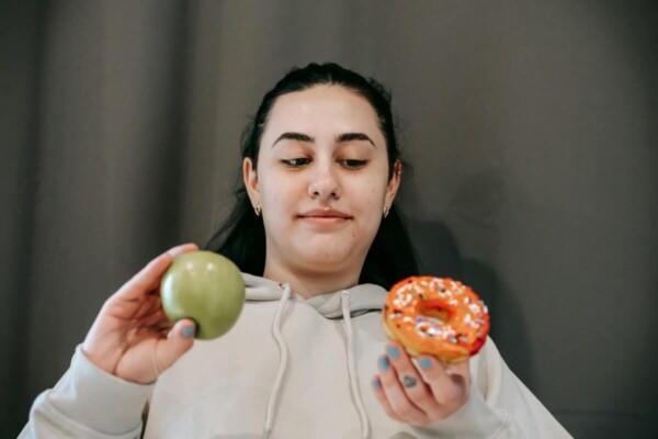 A woman choosing between a donut and an apple