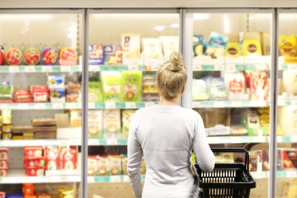 Woman choosing frozen food from a supermarket freezer, reading product information