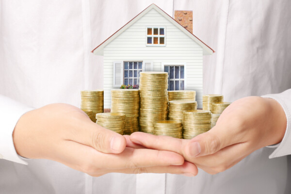 A woman holding a model home and a pile of coins