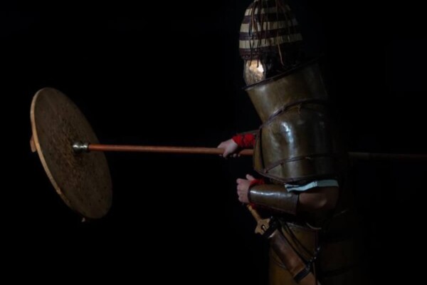Man wearing replica armor and hitting a shield with a spear/staff.