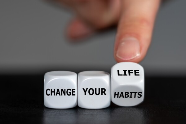 Hand turns dice and changes the slogan 'change your habits' to 'change your life'.