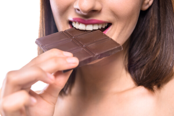 Young woman eating bar of dark chocolate.