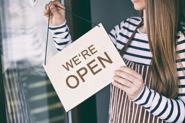 Woman holds the wooden sign with text: we're Open