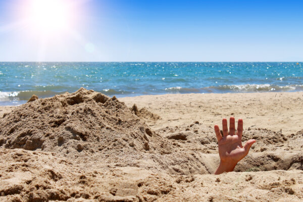 Human hand out of the hole on the sandy beach