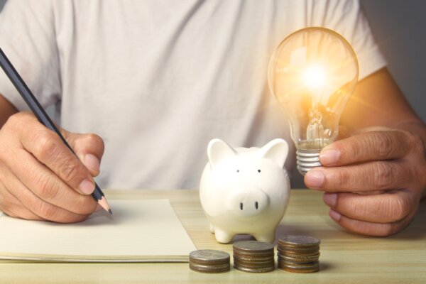 Man holding light bulb with notes with pile of money and piggy bank