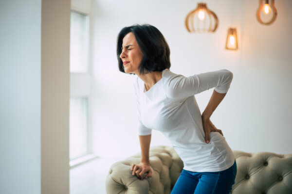 woman is holding her lower back, while standing and suffering from unbearable pain.