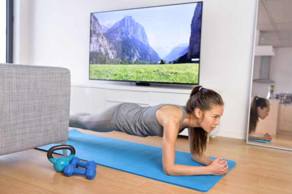 Woman doing plank exercises to exercise core at home watching television.