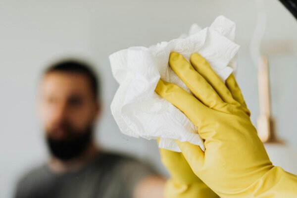 Someone wiping a mirror with a paper towel and rubber glove on